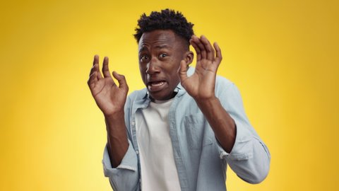 Fear and phobia concept. Studio portrait of young afraid african american guy feeling frightened, screaming and recoiling with open palms, yellow studio background, slow motion