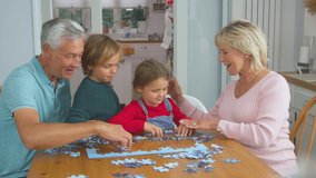 Grandchildren with grandparents sitting around table at home doing jigsaw puzzle together - shot in slow motion - Powered by Shutterstock - Get 15% off with code: PIKWIZARD15