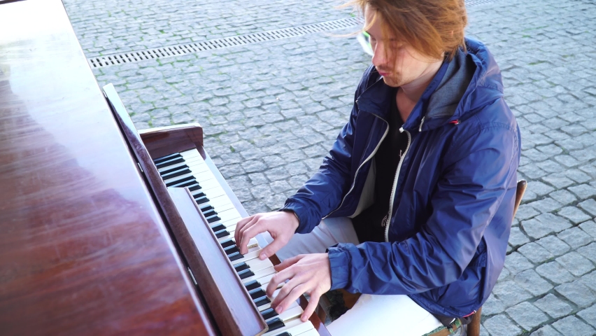 Red-haired guy playing the piano in a blue jacket on the street