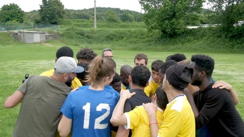 Olot, Spain - 20 june 2021: soccer team of young african migrants and european young men in a huddle having team talk and inciting before match on football pitch