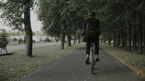Young man riding a bike in the city park wearing suit and a helmet, back view. Businessman riding a bicycle in a public softwood park at the sunset. High quality 4k footage - Powered by Shutterstock - Get 15% off with code: PIKWIZARD15