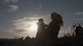 Silhouette of happy mother plays with his son against the sunset, mom with baby shining in backlighting. High quality 4k footage