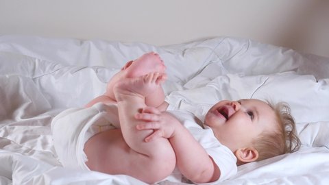 Woman hands tickle adorable 7 month baby girl in white clothes lying on the bed 