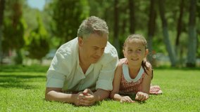 Father and little daughter are lying side by side on the grass. Happy little girl and her father are spending time together lying on the grass. Father-daughter bond. Slow motion video.