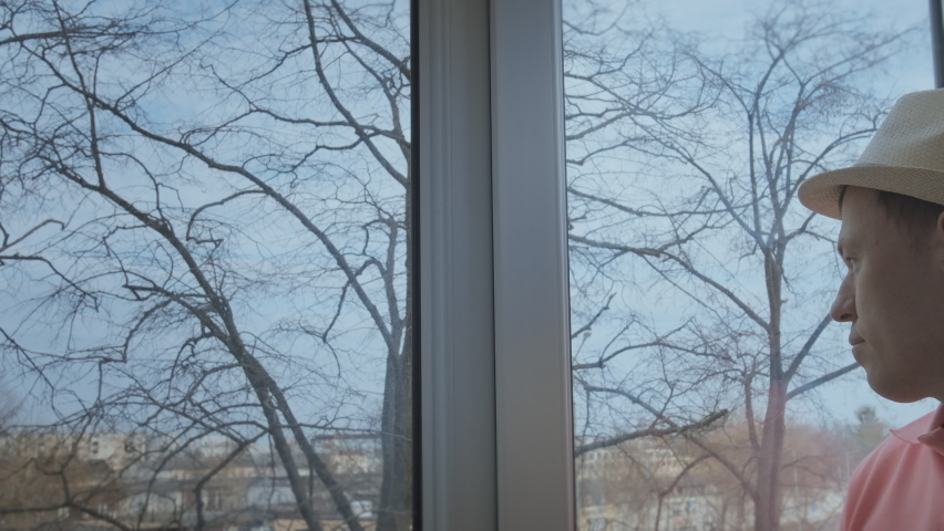 A man looks out the windows to the street, outside the window is a large tree without foliage, autumn time