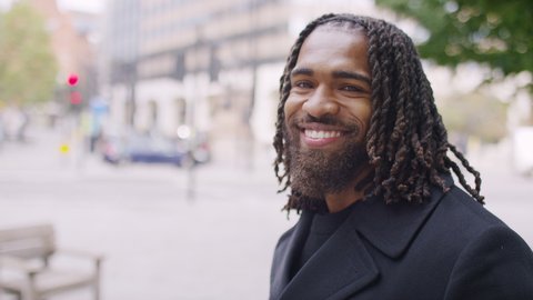 Portrait of handsome black man turning to camera and smiling as he stands in the city, in slow motion