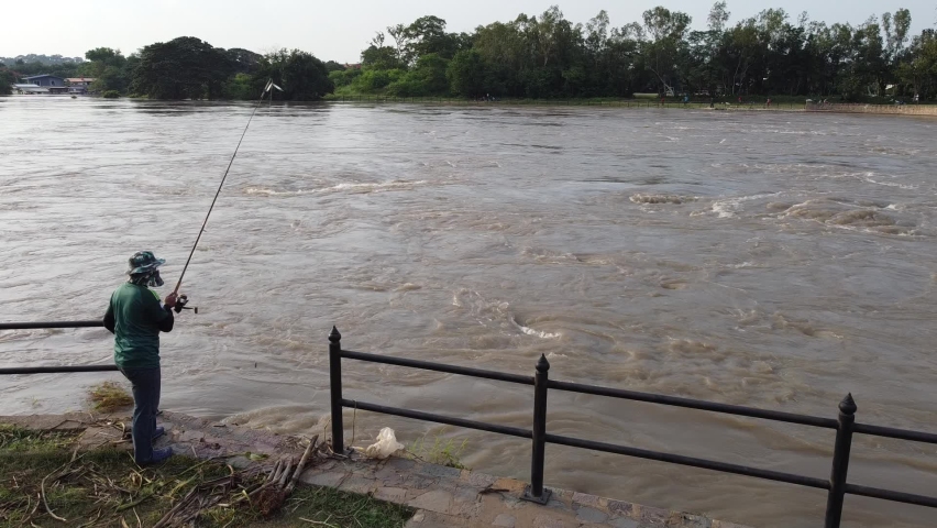 Unidentified Silhouette of a Fisherman with a Fishing Rod at Dam during Flood Situation.