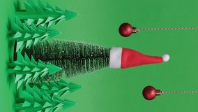 4K. Vertical video. Christmas trees paper artwork in green background. Green fir tree with santa hat rotation. Christmas tree paper cutting design card. New Year background with paper tree - Powered by Shutterstock - Get 15% off with code: PIKWIZARD15