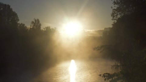 The rising sun has lit up the forest and the fog is floating over the lake on the eve of a warm summer day (it will be a good day)