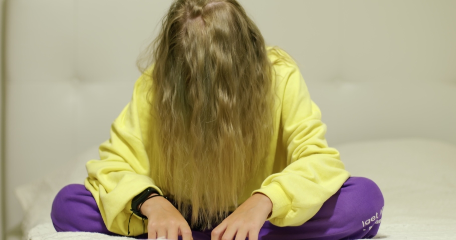 Disheveled teenage girl sitting on the bed at home.
