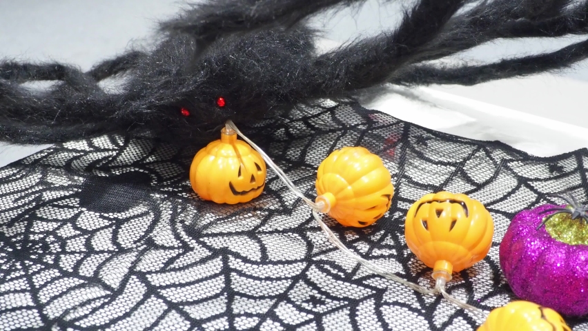 Halloween holiday decorated table with candy and mystery toys, black spider, lantern, decorative pumpkin, selective focus