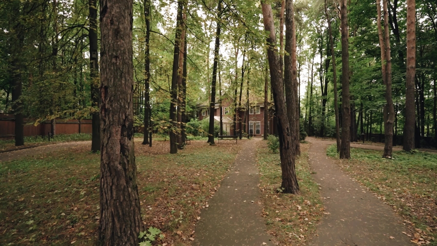 Autumn alley with fallen leaves and a brick house at the end. Shooting in motion