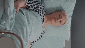 Vertical video: Portrait of sick patient laying in hospital ward bed, looking at camera. Senior woman with nasal oxygen tube and IV drip bag resting to cure diagnosis for healthcare and recovery.