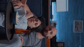 Vertical video: Shocked scared young couple eating popcorn watching movie on tv program at night. Unexpected turn of events in a film. A amazed man and woman are popeyes surprised watching tv sitting