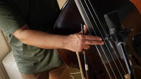 Recording acoustic double-bass in studio. Closeup male hand playing with finger double bass during jazz band rehearsal or recording in studio. 