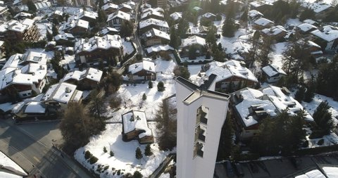Aerial shot of a church at dawn in a beautiful Swiss village covered in snow