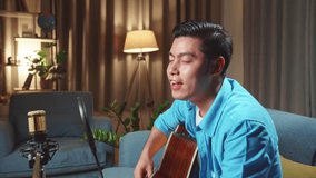 Asian Man Playing Guitar And Sing A Song. The Male Is Streaming For His Social Media Channel. The Man Is Broadcasting Live On The Internet