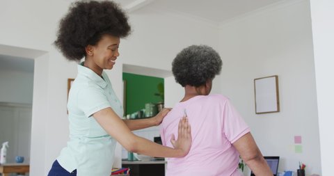 African american female physiotherapist wearing face mask helping senior female patient exercise. senior healthcare and medical physiotherapy treatment during covid 19 pandemic.