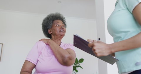 African american female physiotherapist wearing face mask helping senior female patient exercise. senior healthcare and medical physiotherapy treatment during covid 19 pandemic.
