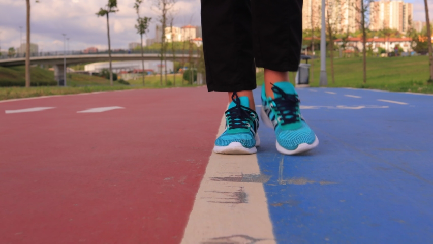 Female feet in green sneakers walk along a red and blue footpath in a park on a summer day