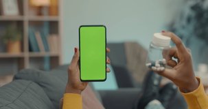 African american woman showing plastic bottle with pills to doctor during video call on modern smartphone. Focus on chroma key screen of mobile. Online consultation concept.