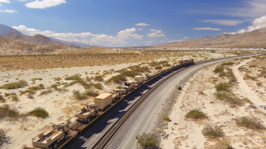 United States Army train transporting military vehicles through the desert, aerial tracking shot as the train passes