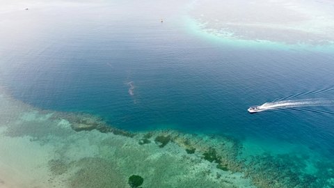 A dive boating through pristine ocean water and coral reefs leaving wake in its trail at stunning remote tropical island getaway. Aerial drone birds eye view of reefs and boat.