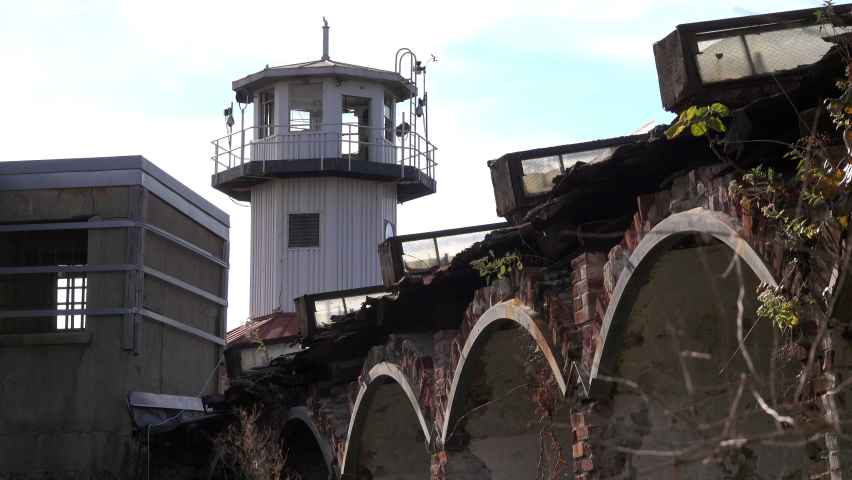 Prison watchtower with dilapidated brick arched wall in foreground.