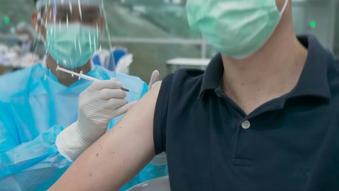 Thai doctor inject vaccine to young white foreigner man. Holding syringe and put needle into a shoulder. Central Vaccination Center Bang Sue station. Slow mo 4k 10bit 422. Bangkok, Thailand
