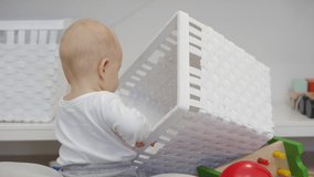 Adorable baby boy learning to crawl and sit having fun exploring all around the house, 7 month old caucasian child on the floor inspecting a white toy box. High quality 4k footage