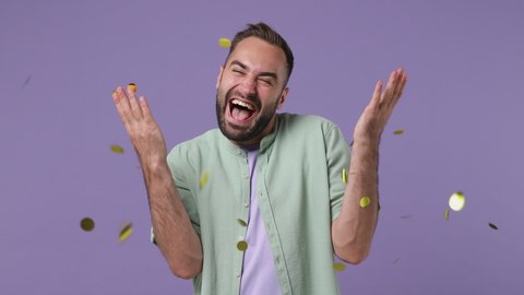 Smiling cheerful happy attractive charming stunning young bearded man 20s years old wear mint shirt hold in hand throw away golden confetti isolated on plain light purple background studio portrait