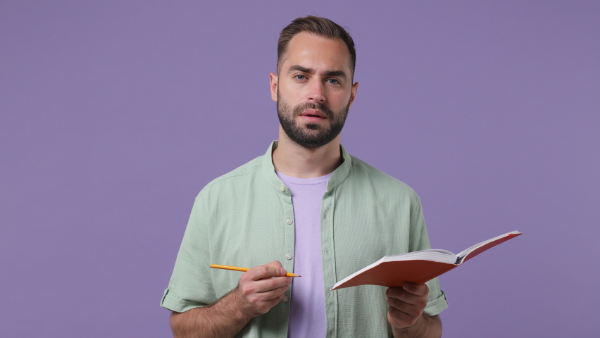 Insighted smart proactive happy confused young bearded man 20s years old wears mint shirt holding pen up with great new idea write in notebook isolated on plain light purple background studio portrait Royalty-Free Stock Footage #1081055462