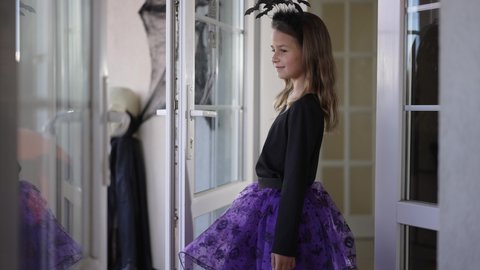 Portrait of cute charming girl spinning posing in Halloween costume with bat headband. Happy Caucasian kid smiling looking at camera standing indoors at home. Traditions and holidays concept