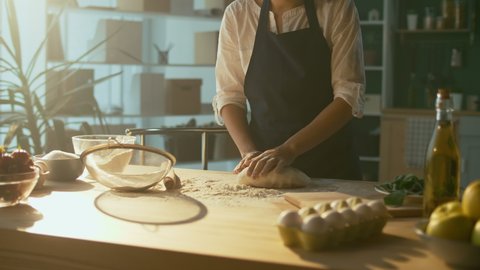 Successful Businesswoman is Happy To Knead the Dough on a Wooden Table in a Cozy Home Kitchen. Woman Baker Enjoys the Process of Making Homemade Cakes. Favorite Work. Small Business.Close-up.