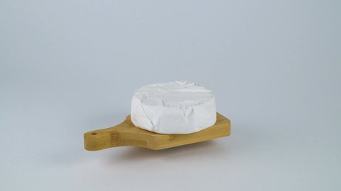Whole head of white brie cheese on a wooden cutting board. Brie cheese rotates on a white plate. Goat dairy product cheese as a delicacy to eat. Mock up template, cope space.
