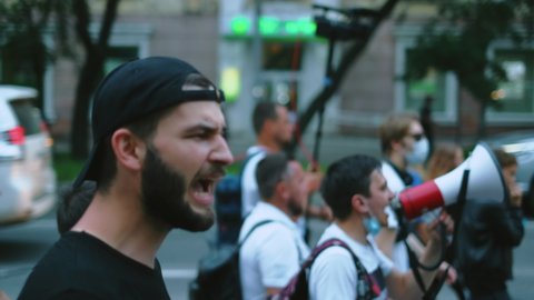 Riot revolt rebel guy in resistance. Strike demonstrator activist male with beard on opposition demonstration protest with background bullhorn megaphone. Protester political man in cap at rally crowd.