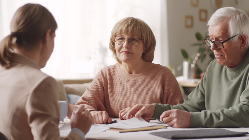 Elderly man and woman sitting at table, reading contract and discussing details with female insurance agent during consultation at home Royalty-Free Stock Footage #1081071866