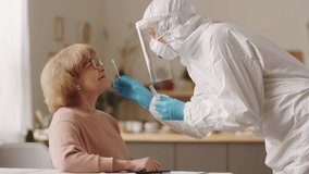 Nurse in protective suit, face shield and gloves taking nasal swab from senior woman, writing something and speaking with patient during at-home covid-19 test - Powered by Shutterstock - Get 15% off with code: PIKWIZARD15