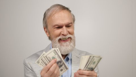Successful senior man counting cash money in studio. Cheerful old aged guy holding currency banknote in hands indoors. Happy retired male person getting wealth by jackpot. Rich retirement investment