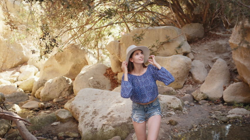 Portrait, Charming caucasian woman wearing summer hat and clothes walking among high rocks and looking around. Female tourist discovering new place during summer adventure. Look at the camera.