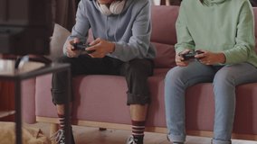 Tilt up shot of teenage boy and girl sitting on sofa, smiling and playing video game on console with excitement