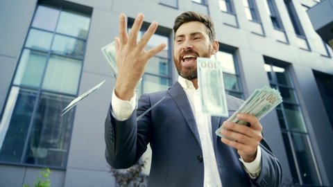 Happy successful Caucasian bearded businessman counts, waves, throws, show off, flaunt cash money background a modern office building looking at camera Celebrate Winner success in betting stock market