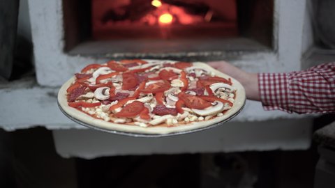 baking pizza in an open fire in a firewood oven. A female hand puts mozzarella pizza in the oven in an iron pan. Baking in pizzeria.