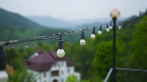 Stretched cord with light bulbs outdoors on a background of mountain nature in rainy cloudy weather. Change of focus. Switching focus from light bulb to light bulb.