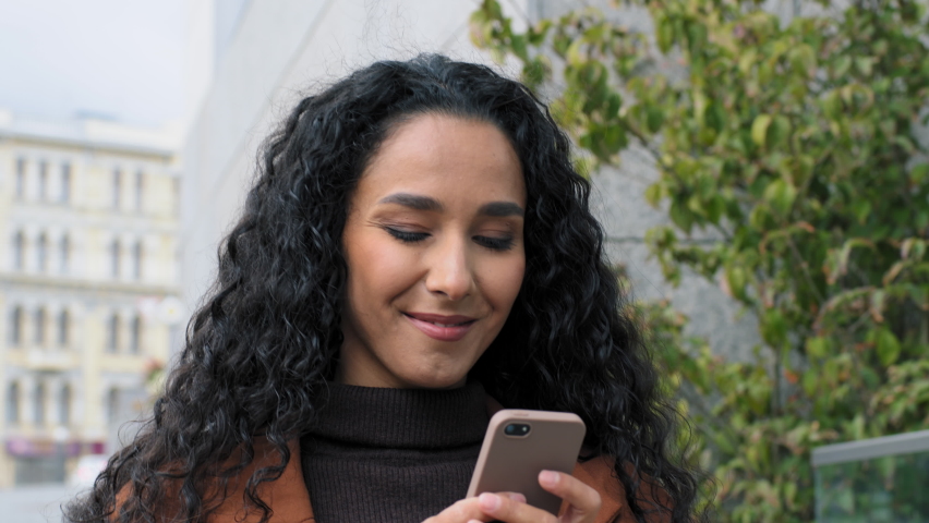 Happy latin hispanic girl young business woman walking in city street looking into mobile phone smartphone screen chatting online in net smiling answering message in social media using gadget device | Shutterstock HD Video #1081089221