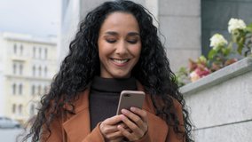 Happy latin hispanic girl young business woman walking in city street looking into mobile phone smartphone screen chatting online in net smiling answering message in social media using gadget device - Powered by Shutterstock - Get 15% off with code: PIKWIZARD15