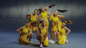 Group of beautiful , funny, stylish girls in yellow dresses dancing inside pavilion with grey background  . Synchronized dance of female ensemble for video clip  Woman dancers with the same outfit 