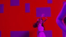 Group of beautiful , funny, stylish girls in white same dresses dancing inside decorated pavilion  with purple cubes and red  wall background . Synchronized dance of female ensemble for video clip  