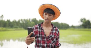 Front view,Young adult farmer wearing Plaid shirt and hat making selfie portrait and video call, smile and looking at the camera with waving hand. Rice field on background