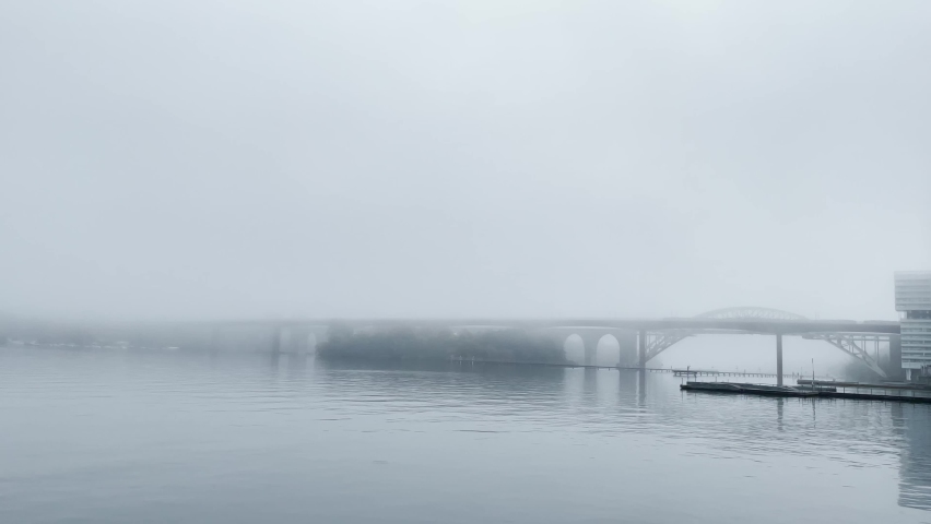 Morning mist in the city and the water with the fog almost hiding the bridge. Cloudy weather this cold day. Footage made in Stockholm, Sweden.